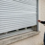 Un volet roulant Bubendorff de travers dans ses coulisses, devant une fenêtre de maison.